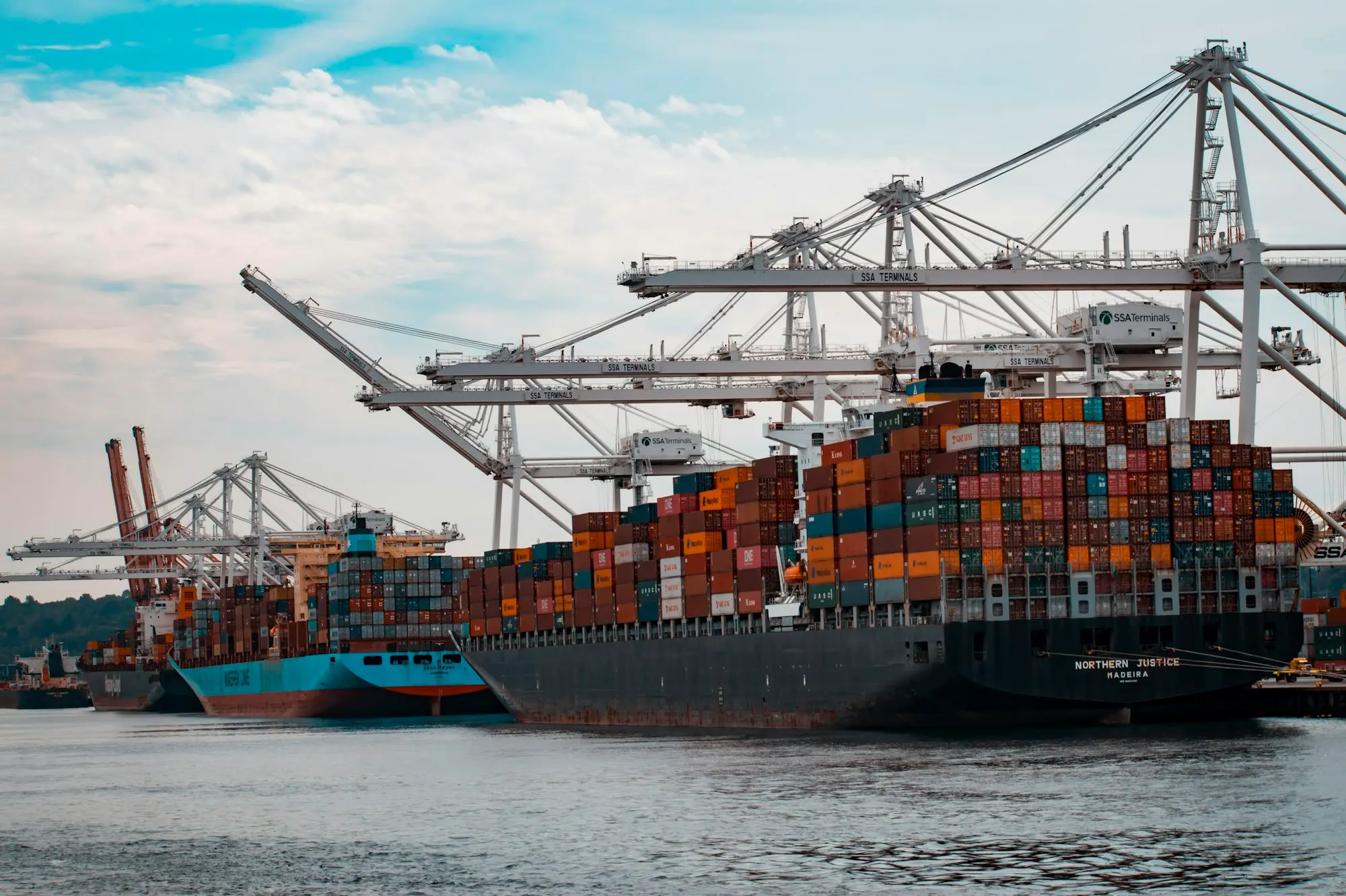Loaded container ships at berth under gantry cranes, waiting for cargo to be discharged and released